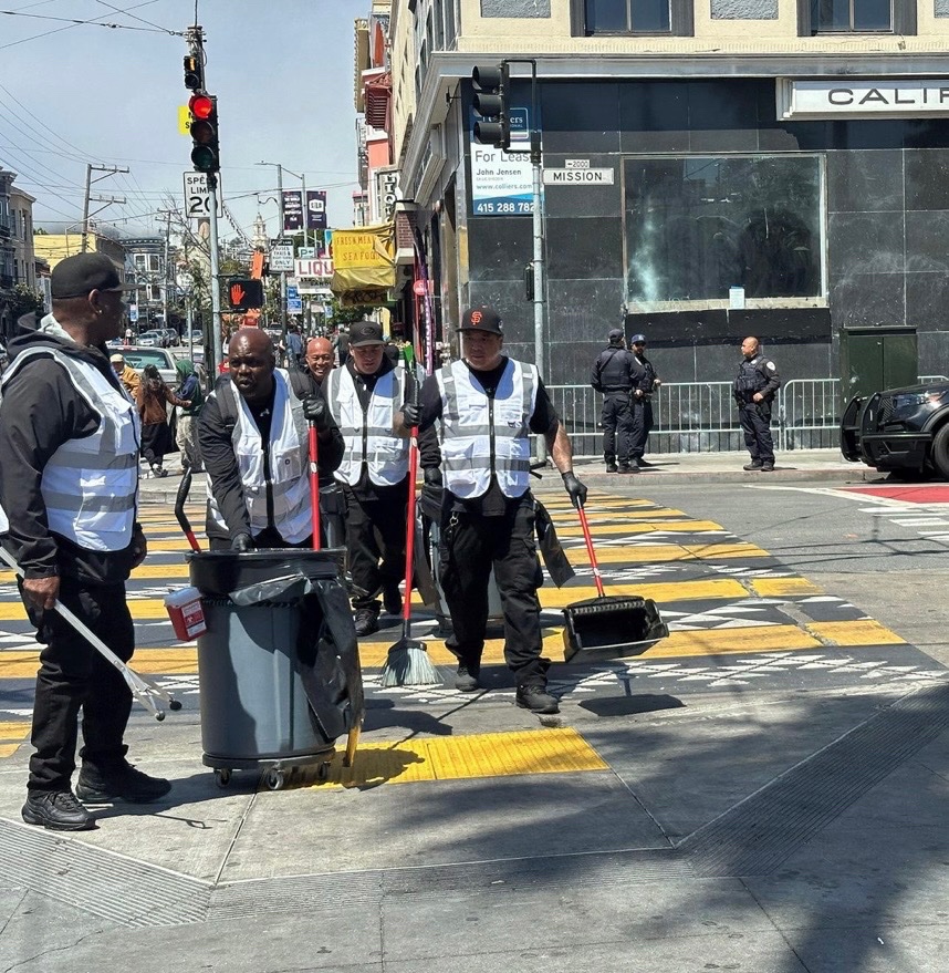 Community Ambassadors walking across a crosswalk with cleaning equipment.
