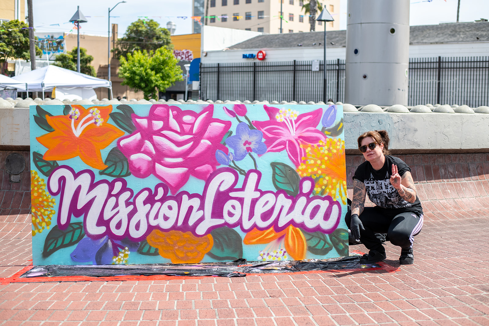 An artist poses with a colorful Mission Lotería mural painted at the plaza