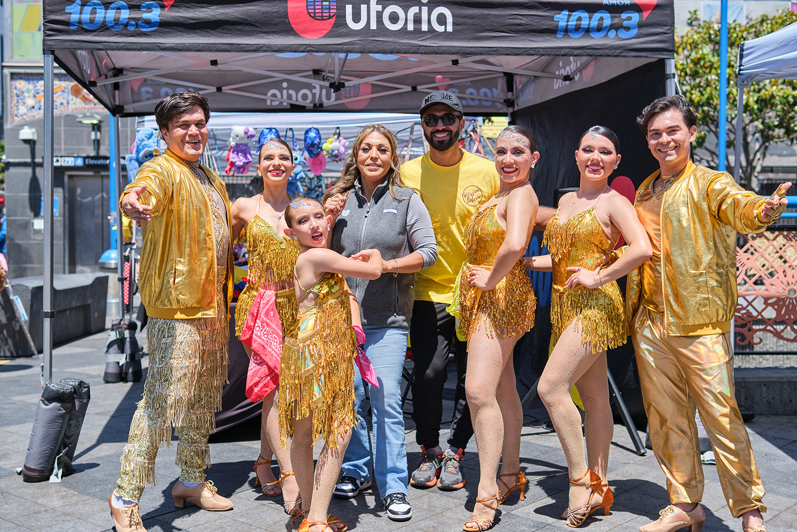 Dance troupe in gold costumes poses with community members at the Sábado Gigante activation